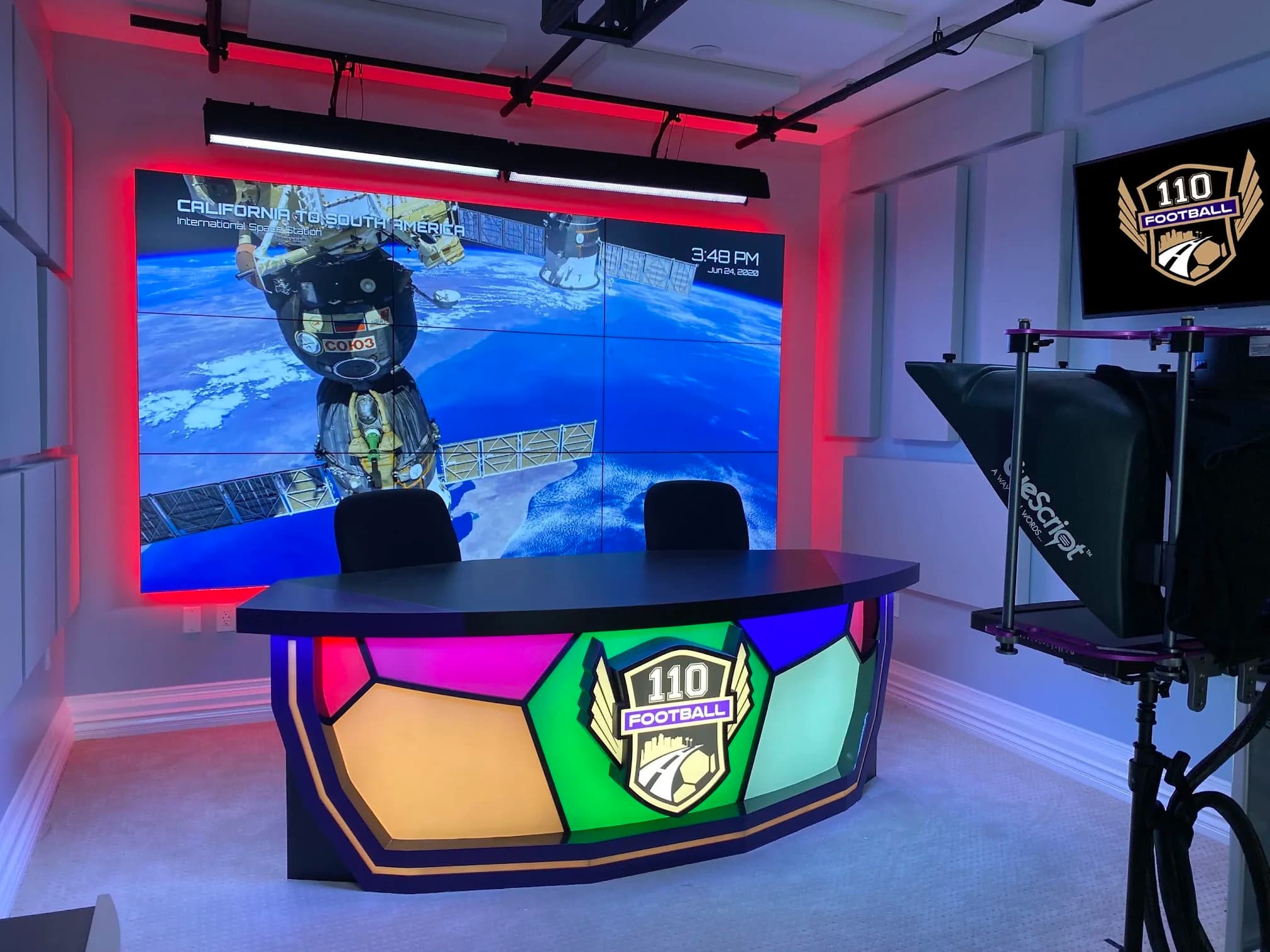 Finished 110 Football studio with illuminated anchor desk, display wall, cameras, and teleprompter