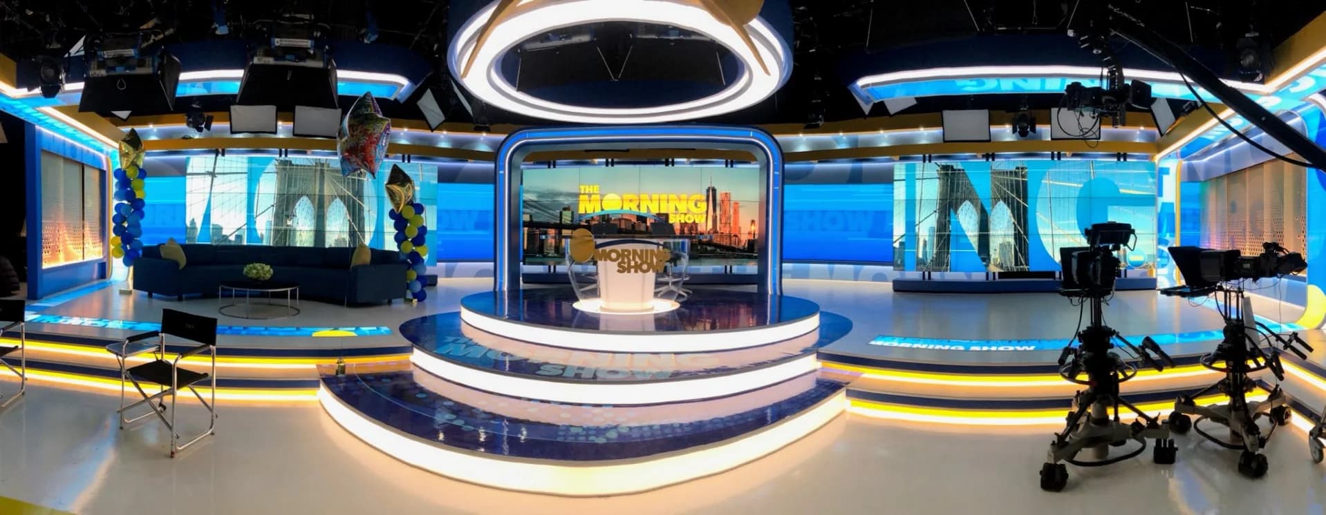 The Morning Show studio with anchor desk, camera pedestals, curved displays, and illuminated scenic elements